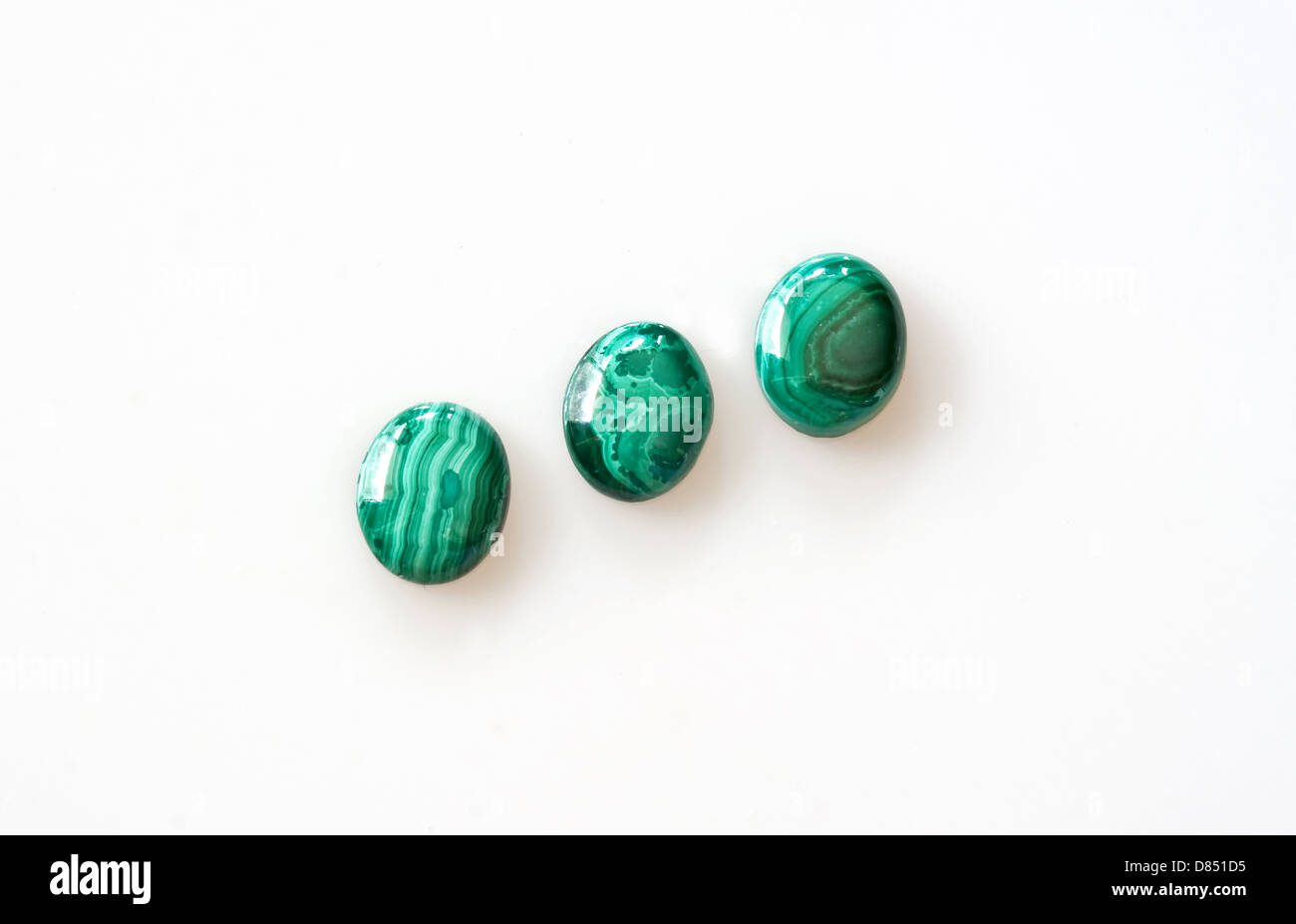3 oval shaped malachite gems, isolated on a light background. It is a copper carbonate hydroxide mineral noted by its green band Stock Photo