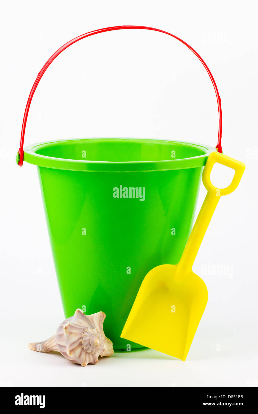 A green sand bucket with a yellow shovel and a whelk seashell. Stock Photo