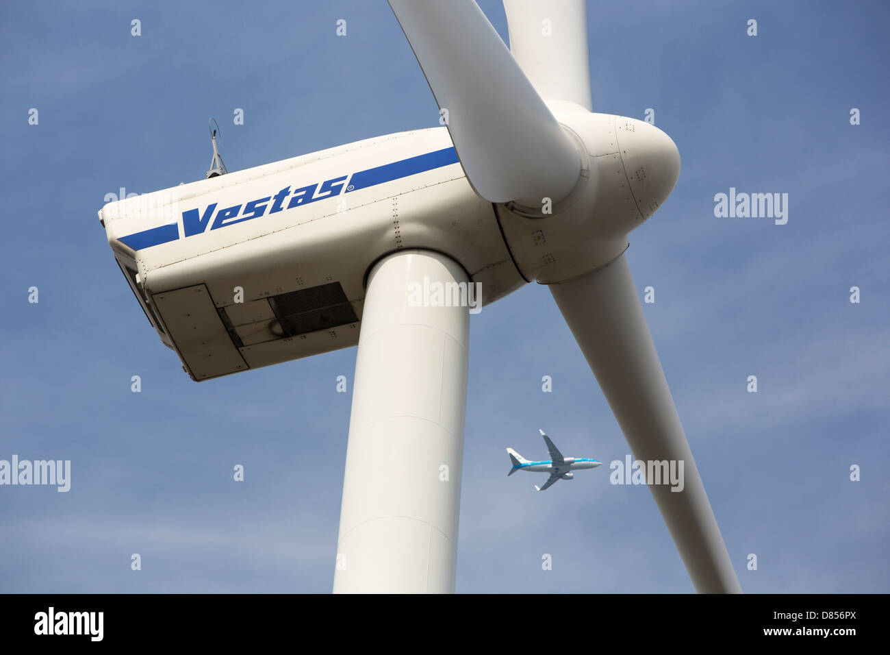 A wind turbine in Amsterdam with a plane flying past having taken off