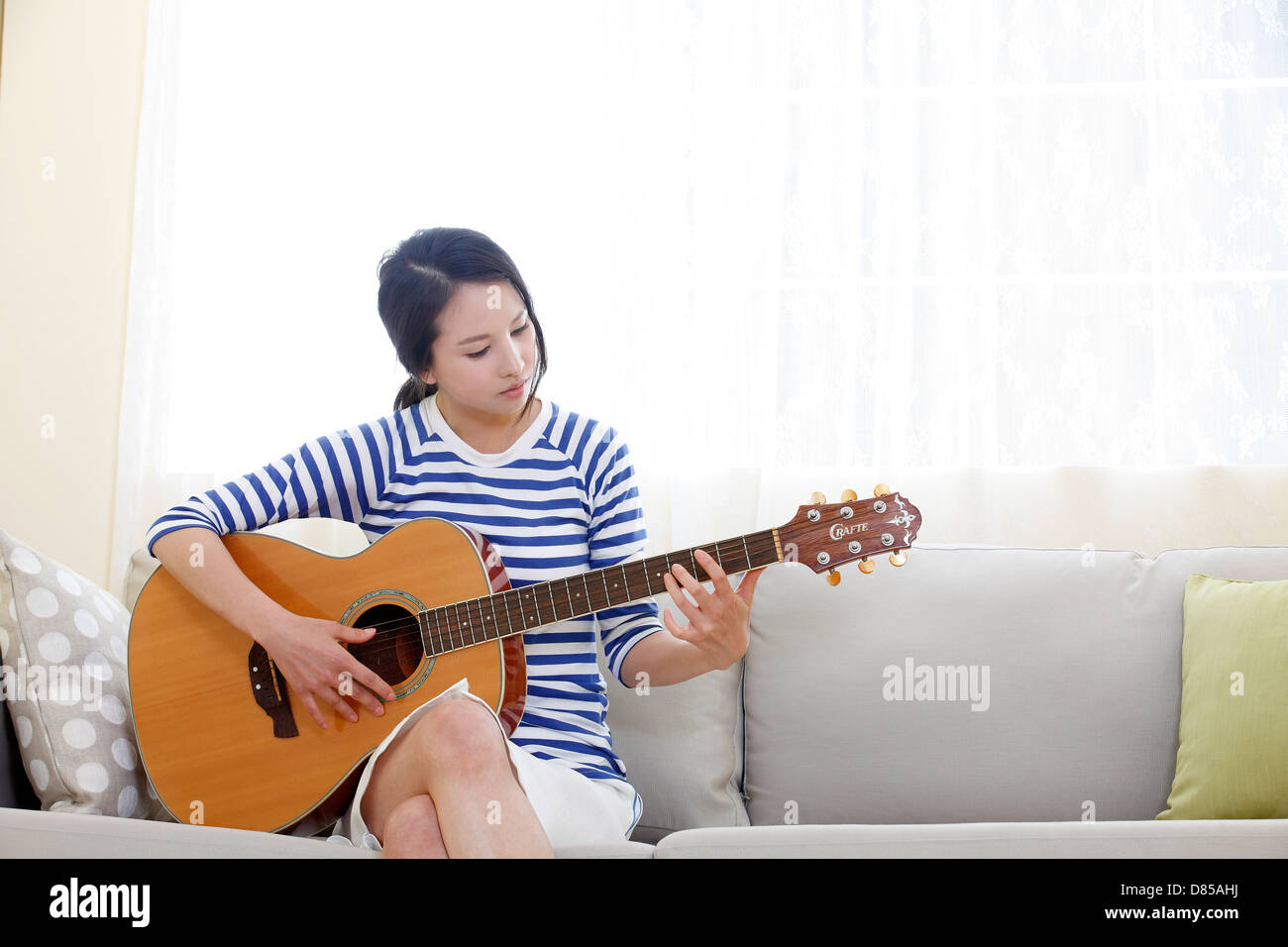 young woman sitting on sofwith acoustic guitar. Stock Photo