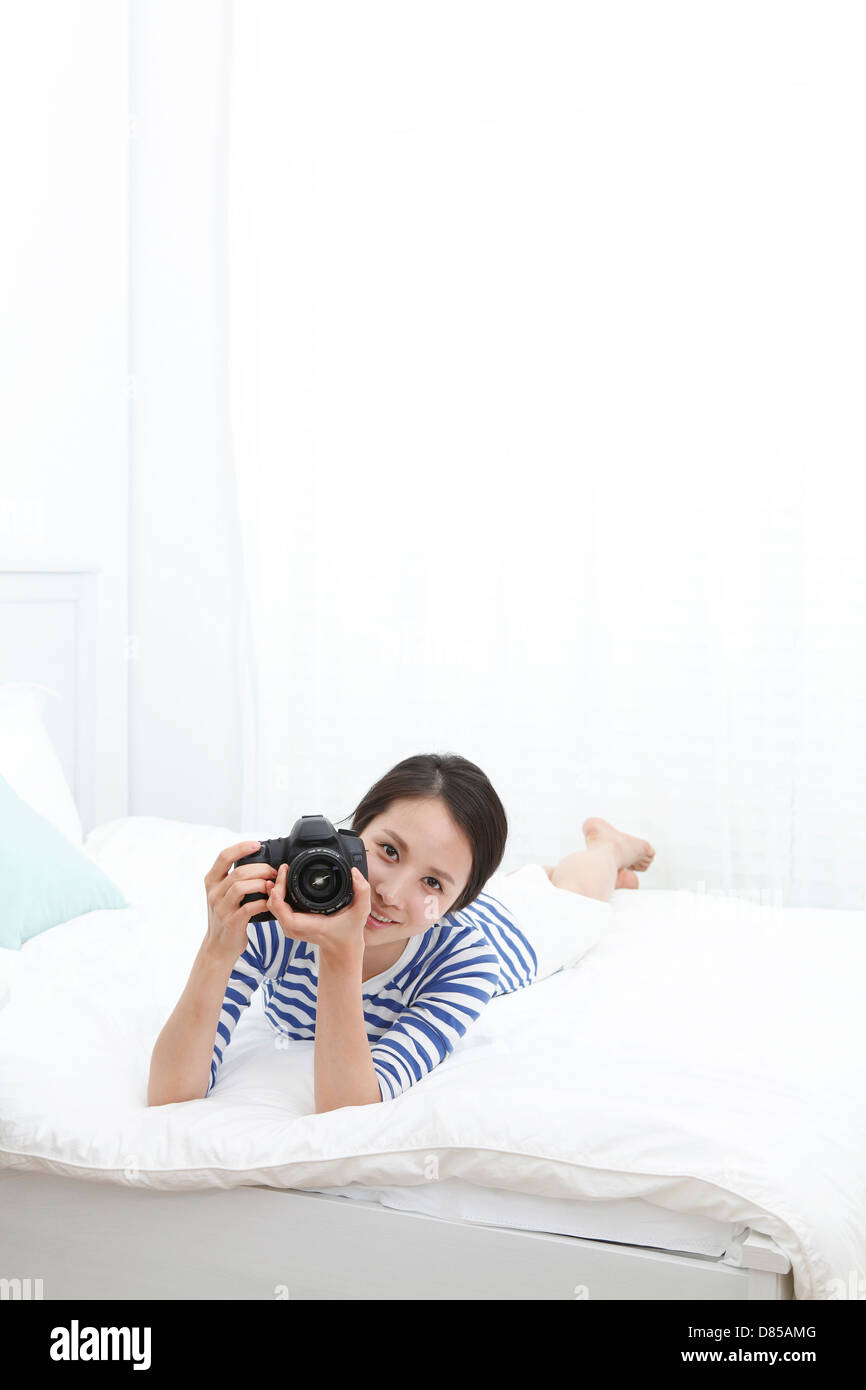 young woman lying on bed holding camera. Stock Photo