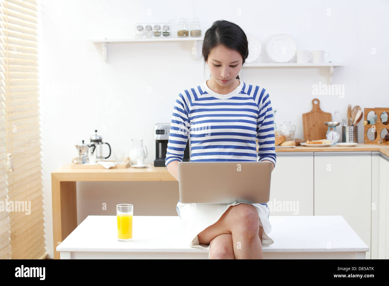 young woman sitting on kitchen table laptop. Stock Photo