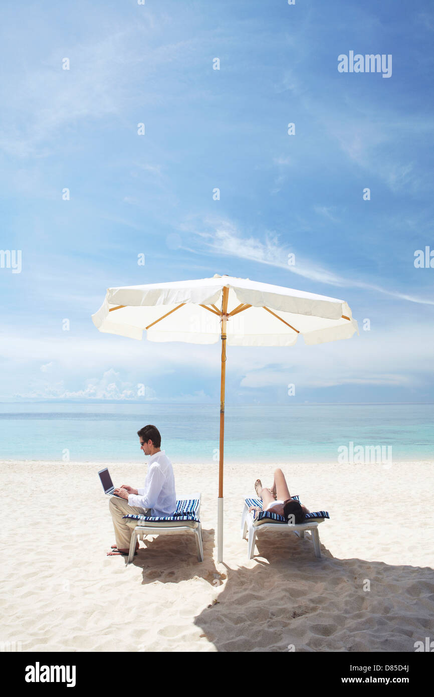 couple relaxing in deck chairs on beach. Stock Photo