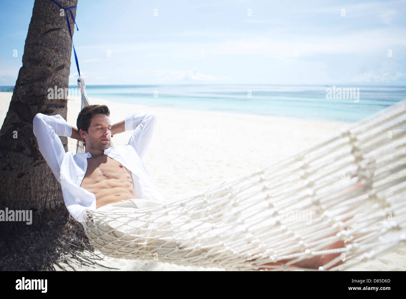 man relaxing in hammock on beach. Stock Photo