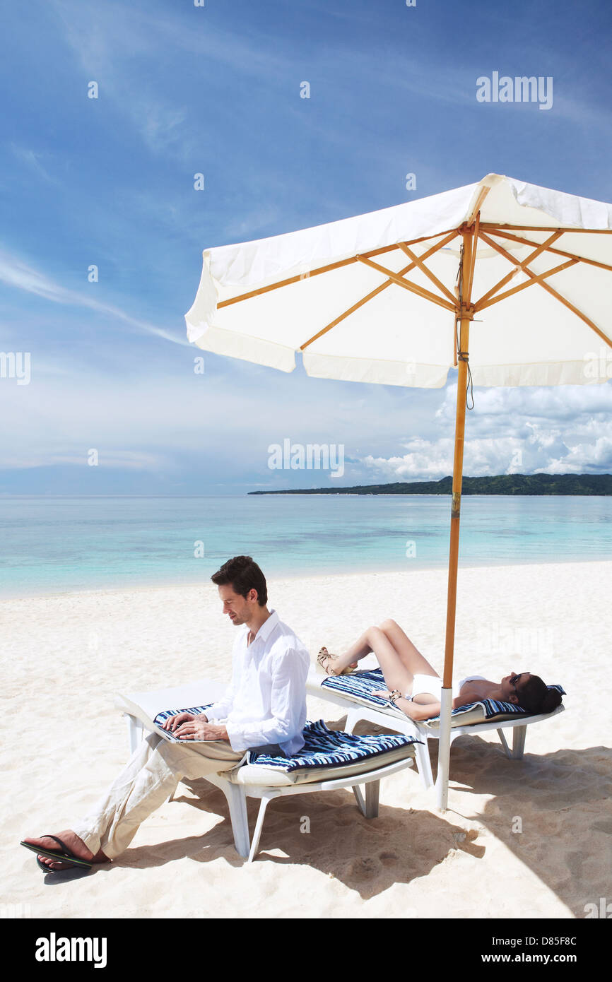 A man working on a laptop in a deck chair on the beach. Stock Photo