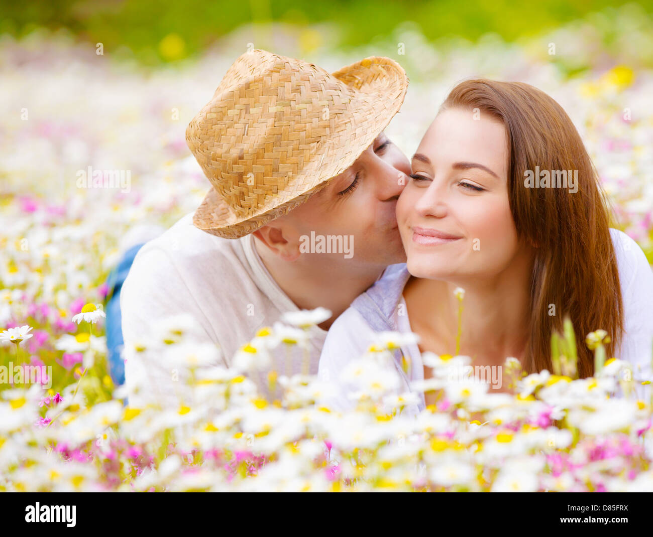 Two happy lovers laying down on white floral meadow, handsome guy kissing his cute girlfriend, relaxation outdoor Stock Photo