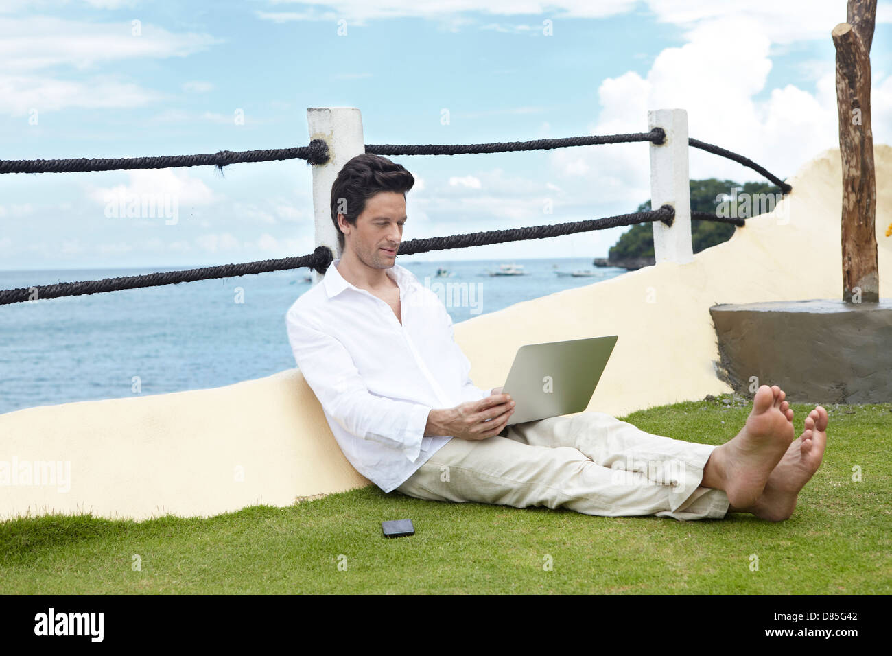 man sitting on grass working on laptop. Stock Photo