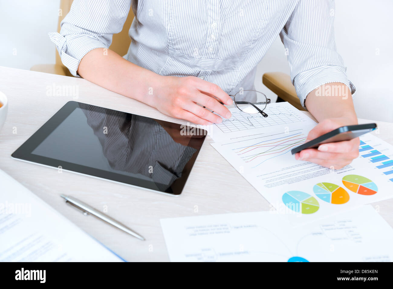 Young successful businesswoman sitting at desk in the office and using mobile phone for business communication Stock Photo