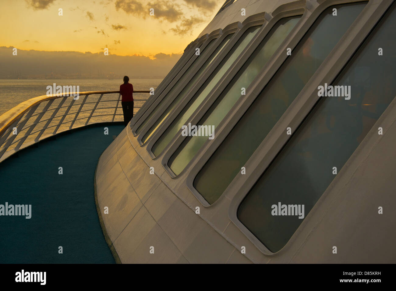 A woman standing on the deck of a cruise ship and watching a sunset ...
