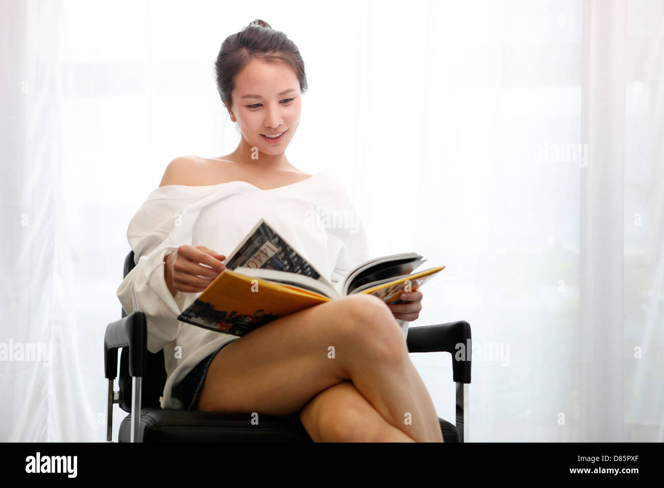 young woman sitting in chair reading book Stock Photo - Alamy