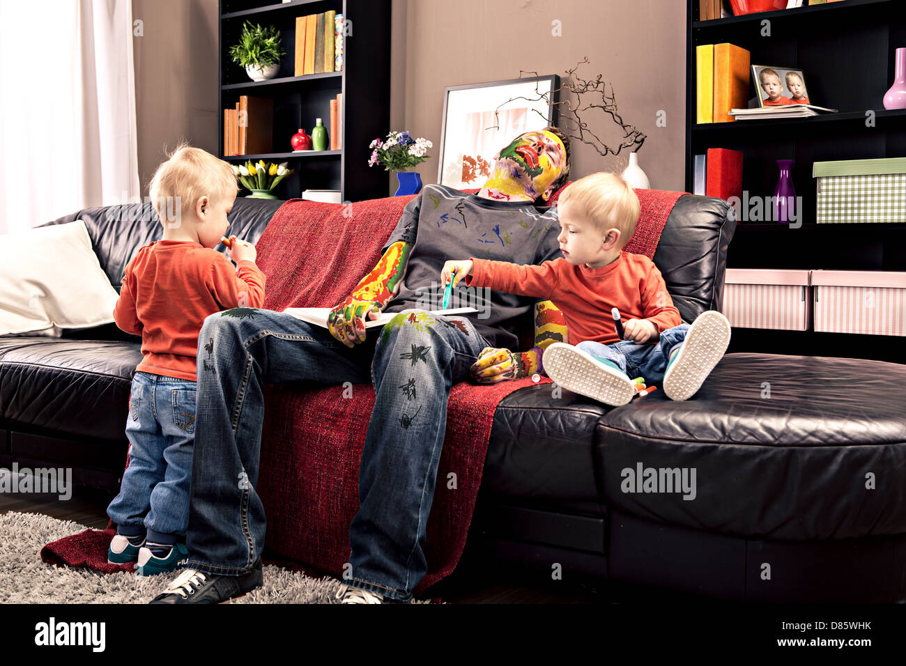 two toddler twins painting on their sleeping father Stock Photo