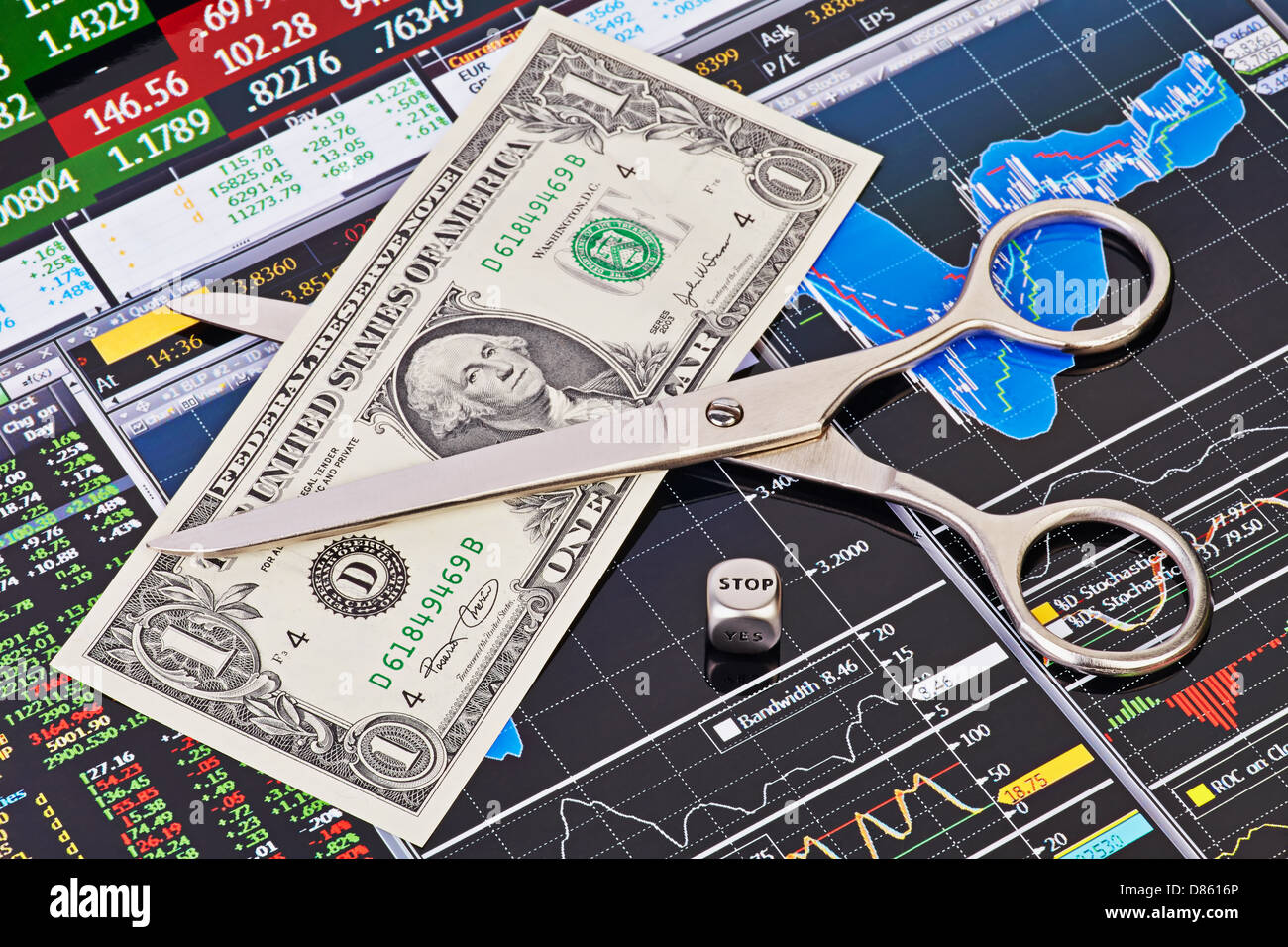 Scissors cutting  one-dollar banknote, dices cube with the word STOP. Financial charts and columns of prices as background Stock Photo