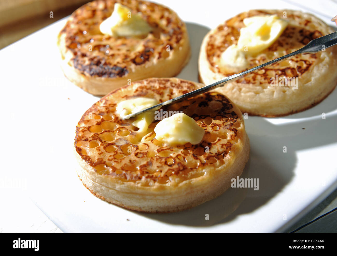 Spreading butter with a knife on a hot toasted crumpet for breakfast or