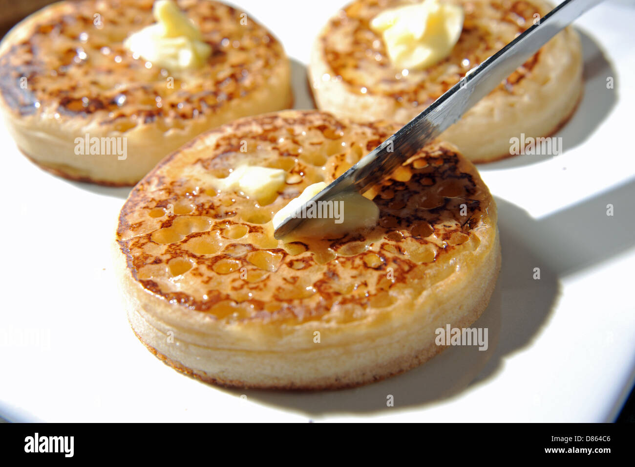 Spreading butter with a knife on a hot toasted crumpet for breakfast or tea Stock Photo