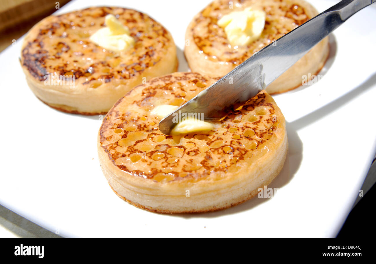 Spreading butter with a knife on a hot toasted crumpet for breakfast or tea Stock Photo