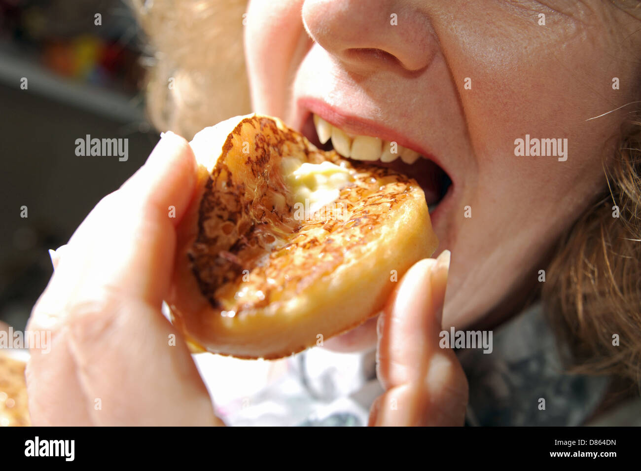 Woman enjoying eating a hot buttered crumpet for breakfast or tea Stock Photo