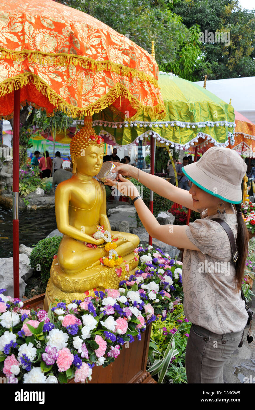 Thai lady pours water over a golden seated buddha statue during Songkran at Wat Po, temple of the reclining buddha in Bangkok. Stock Photo