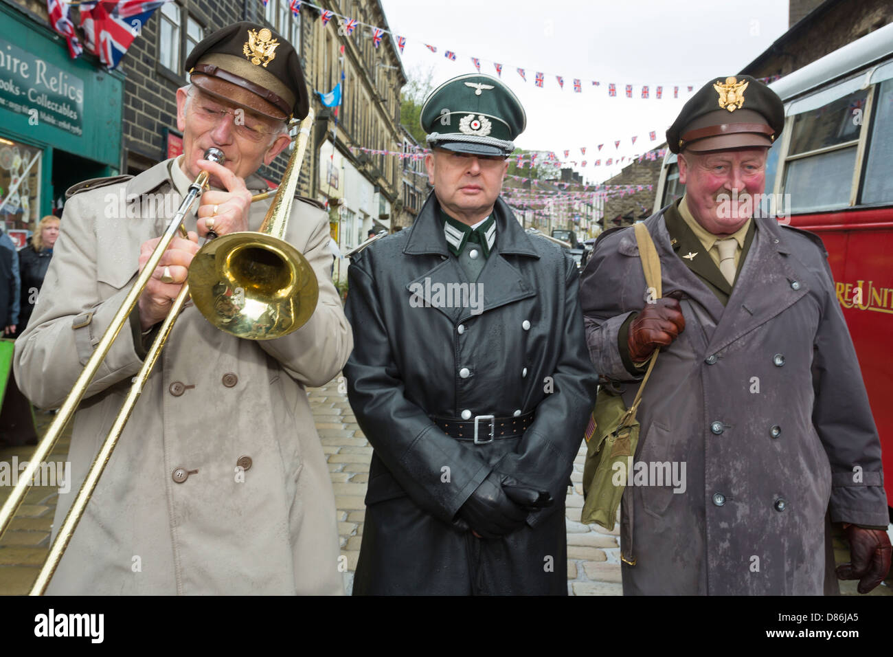 Two men in American Army uniforms, one playing a trombone, with a man in Germany Army uniform. Haworth 1940s weekend, May 2013. Stock Photo