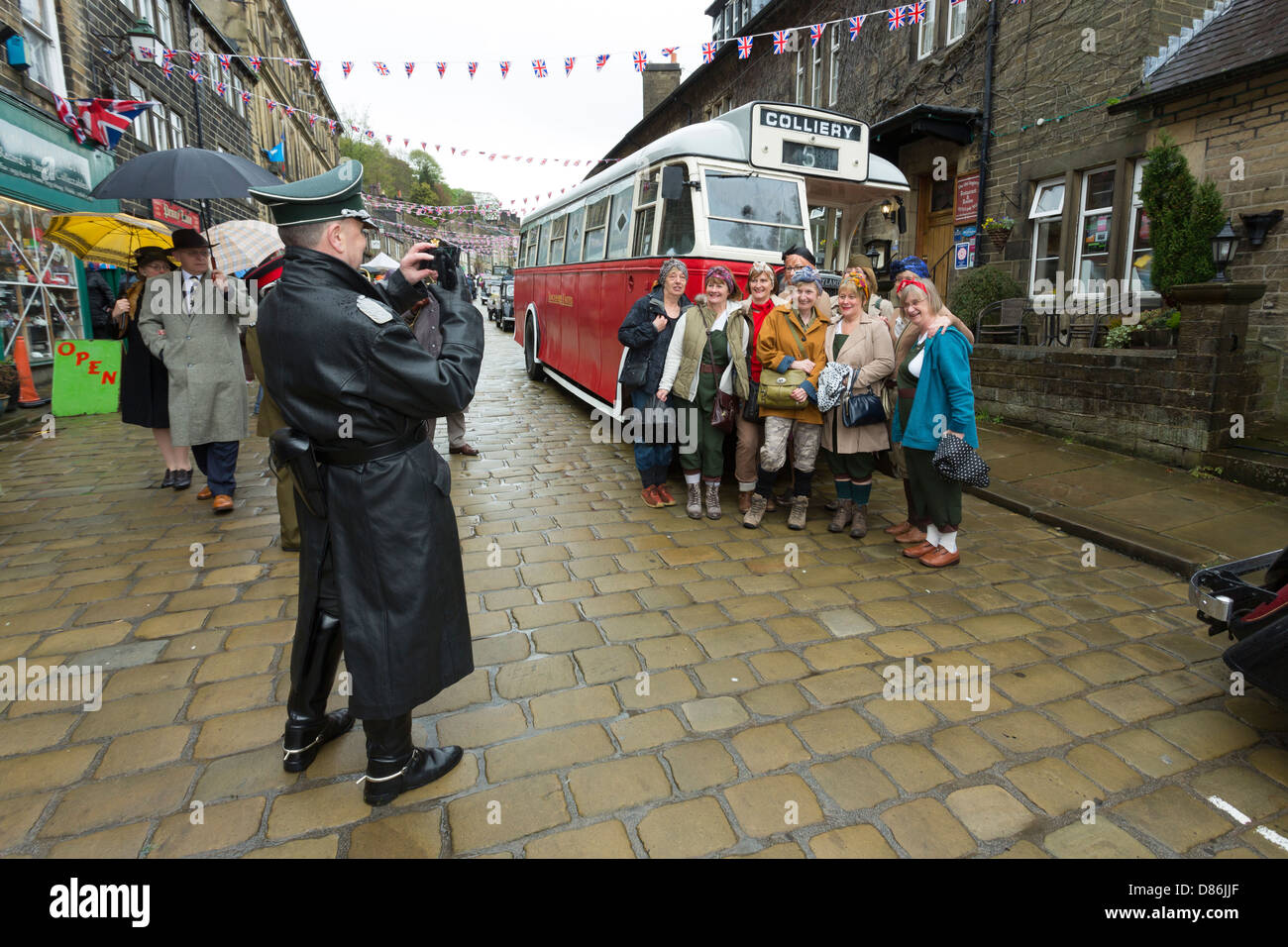 A man in German Army uniform photographing a group of women dressed as land girls in front of a bus. Haworth 1940s weekend. Stock Photo