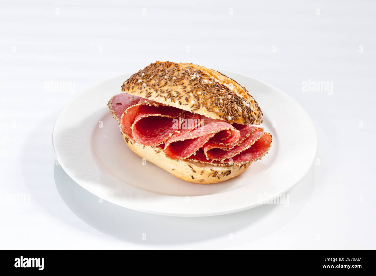 Sandwich of caraway seed bread roll with pepper salami on plate, close