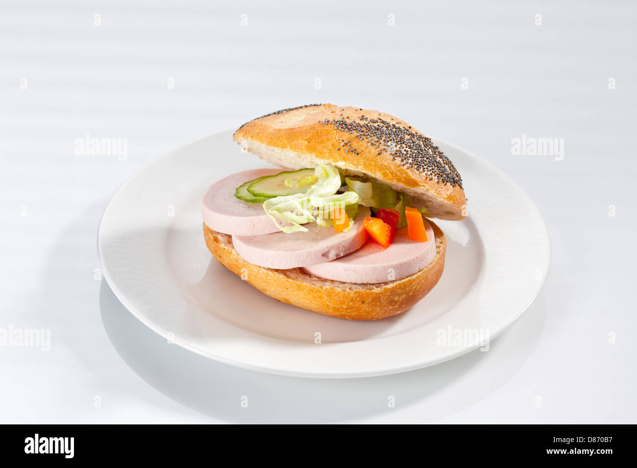 Sandwich of poppy seed bread roll with ham sausage on plate, close up