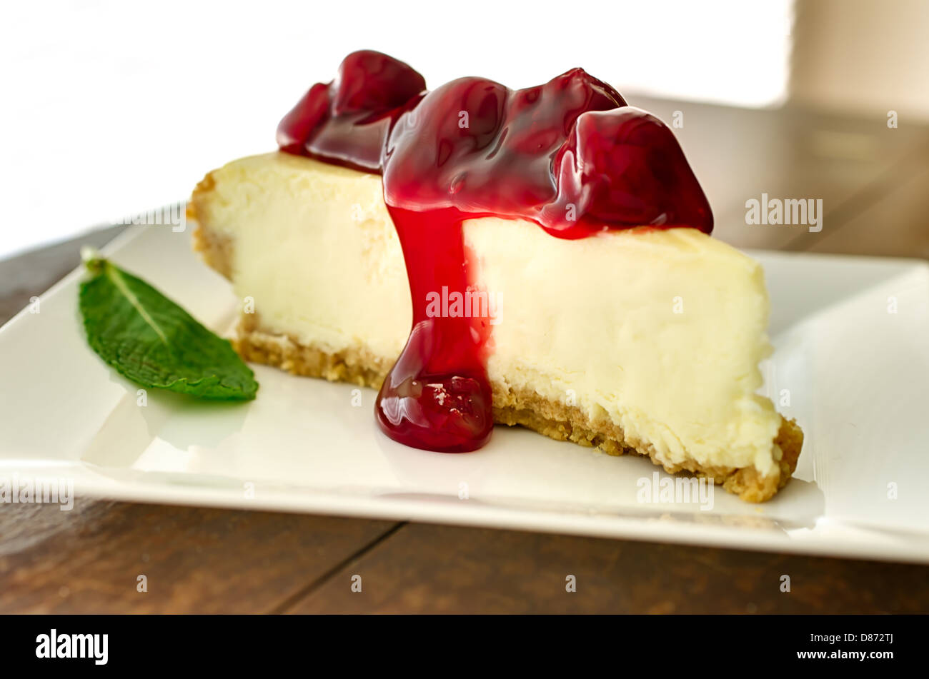 Slice of cherry cheesecake in the afternoon with mint garnish. Shallow depth of field. Stock Photo
