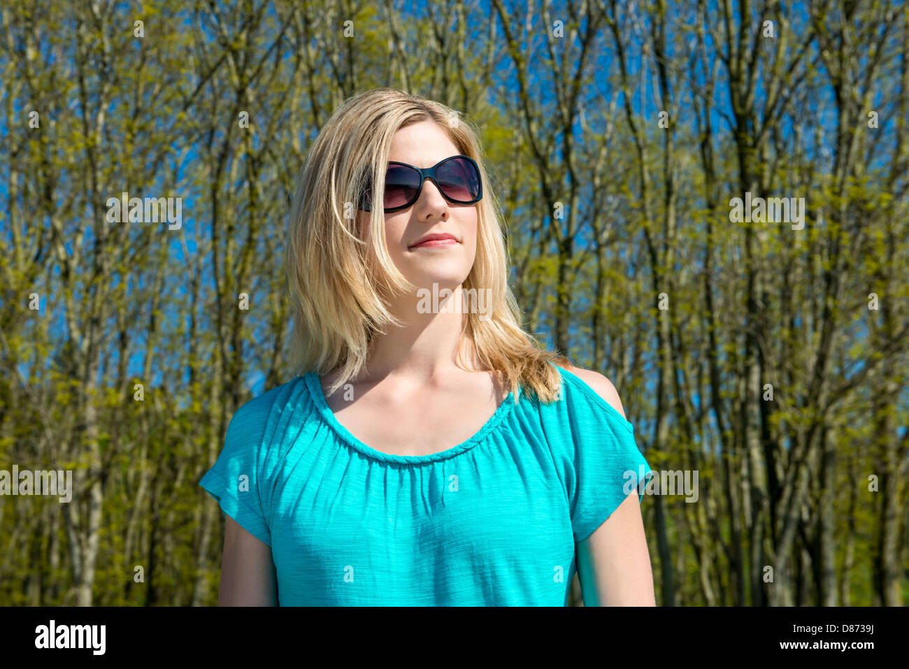 Front view of beautiful young woman wearing sunglasses standing against trees Stock Photo