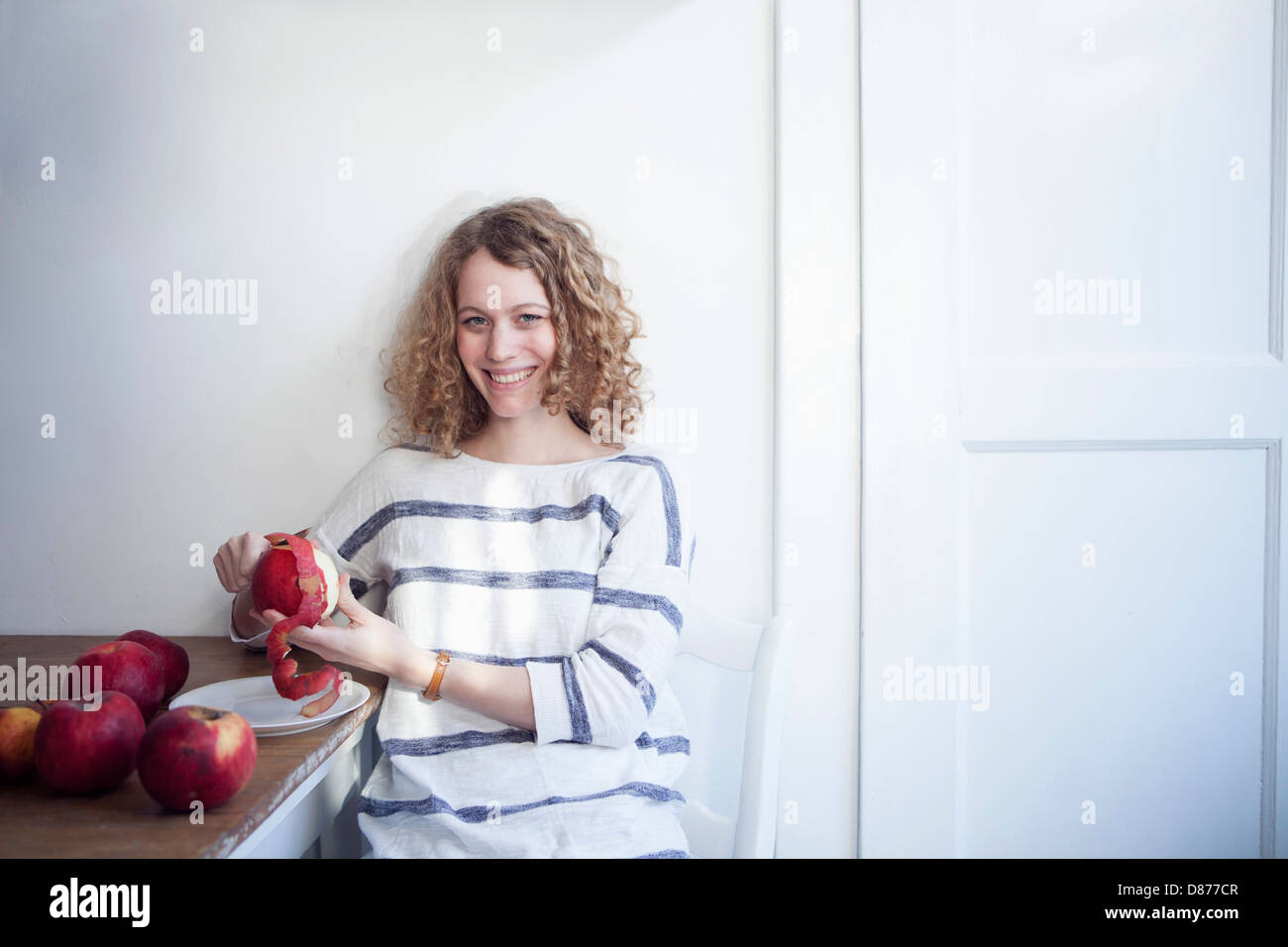 Germany, Bavaria, Munich, Young woman sitting at table and peeling apples, smiling Stock Photo