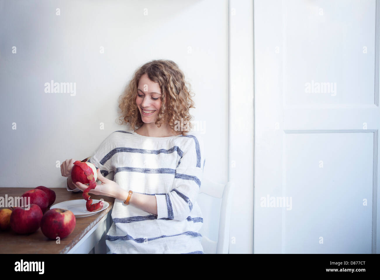 Germany, Bavaria, Munich, Young woman sitting at table and peeling apples, smiling Stock Photo