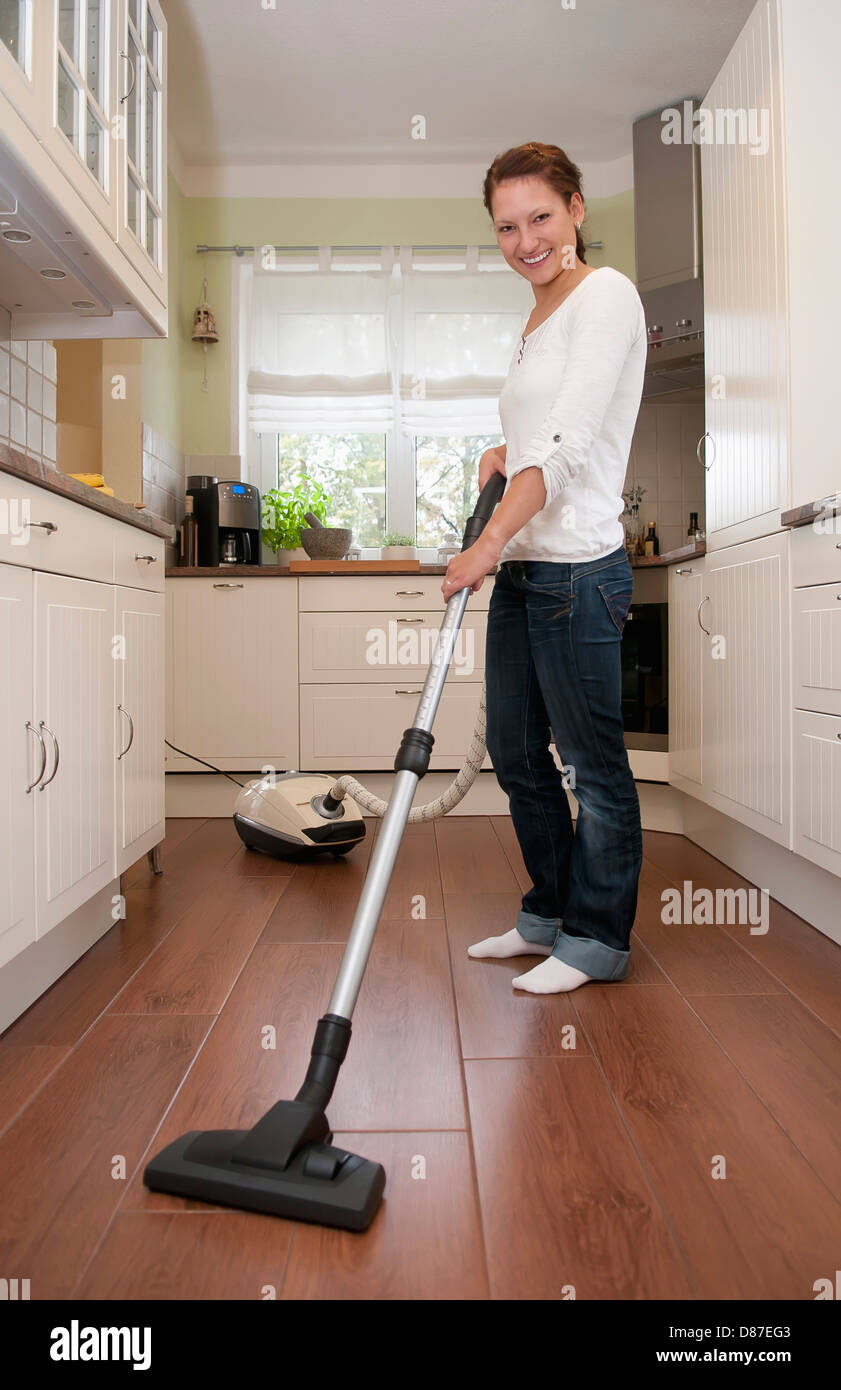 Germany, Brandenburg, Young woman cleaning floor with vacuum cleaner