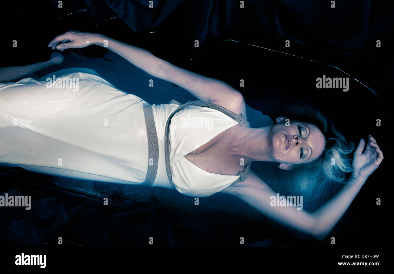 Woman in white dress laying in pool of black water Stock Photo