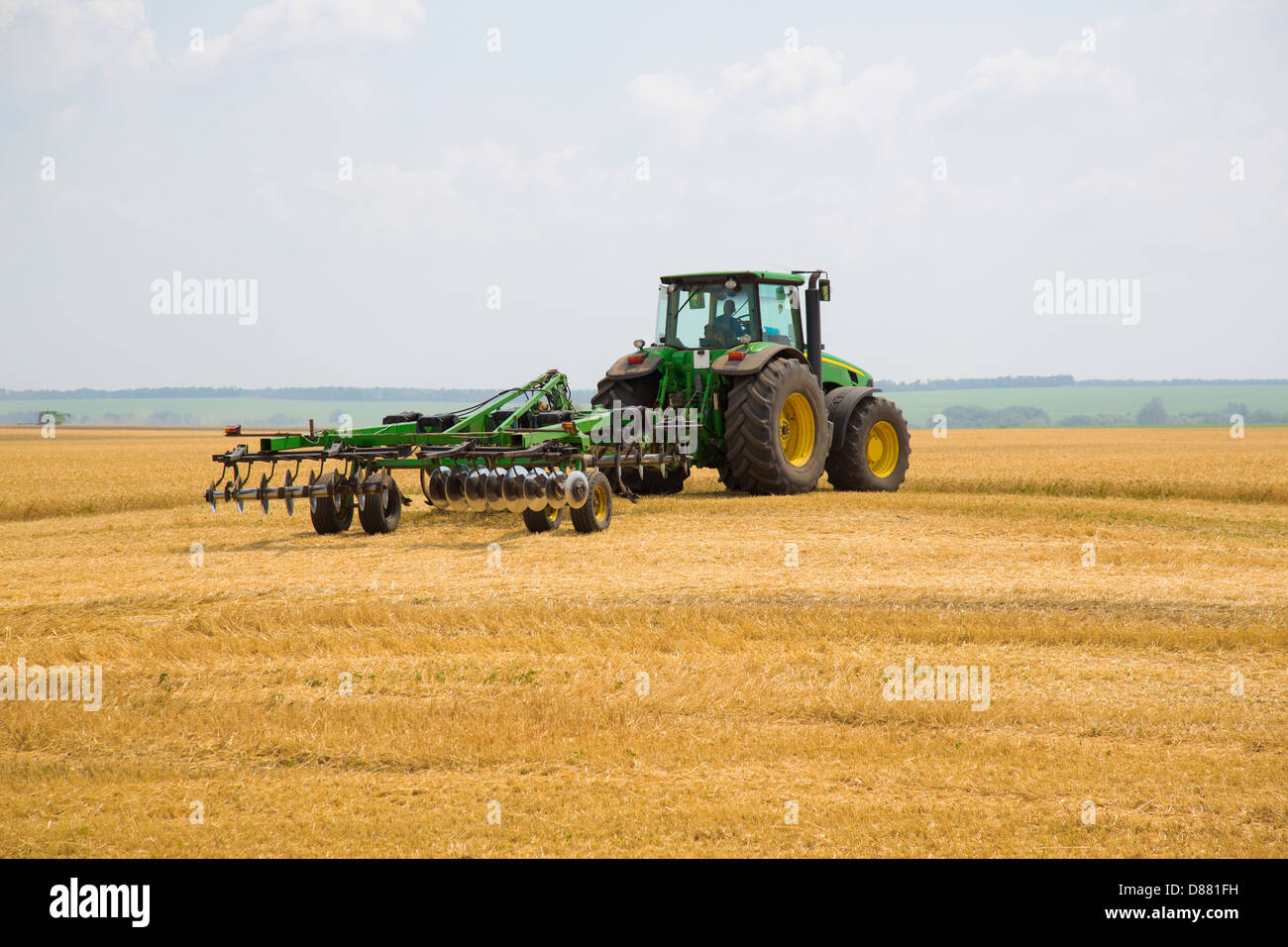 Tractor linked up with a cultivator on a harvesting of a ripe wheat field Stock Photo