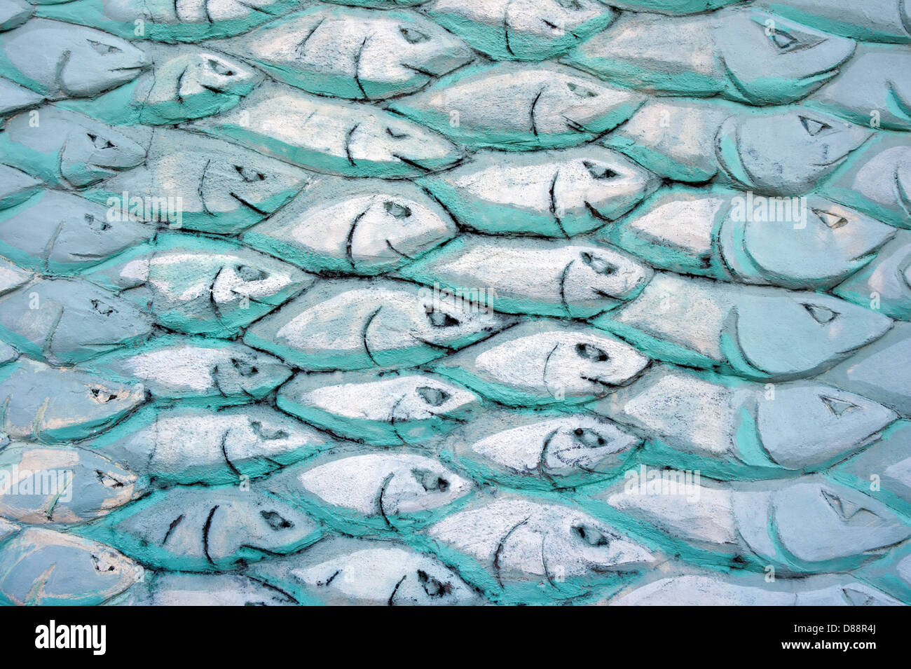 A shoal of fish carved in plaster on a wall and painted with tones of blue, green and turquoise. Stock Photo