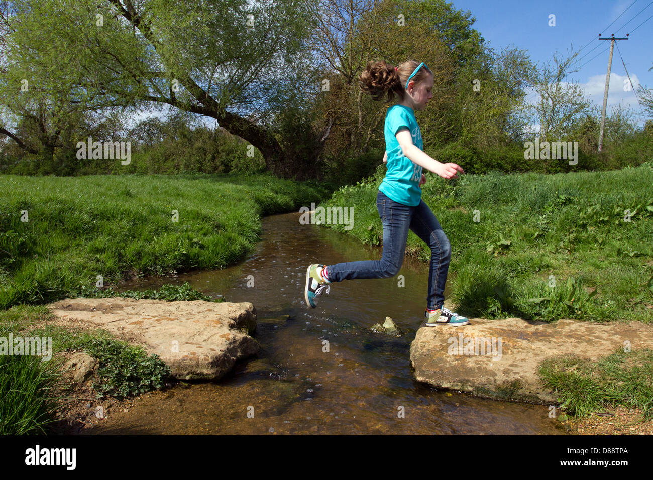 young girl jumping over a stream Stock Photo
