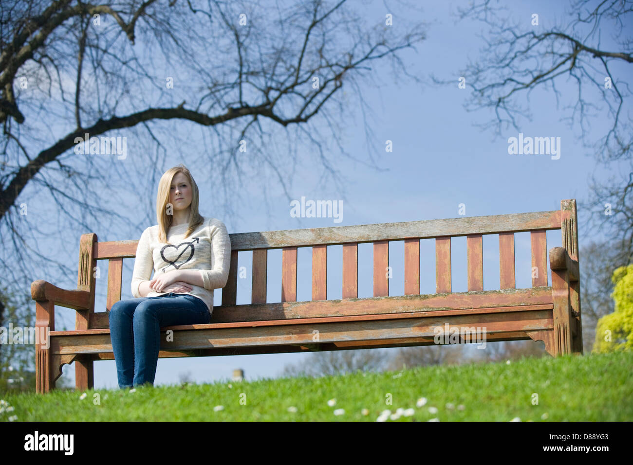 A Young woman sitting on a park bench by herself. Stock Photo