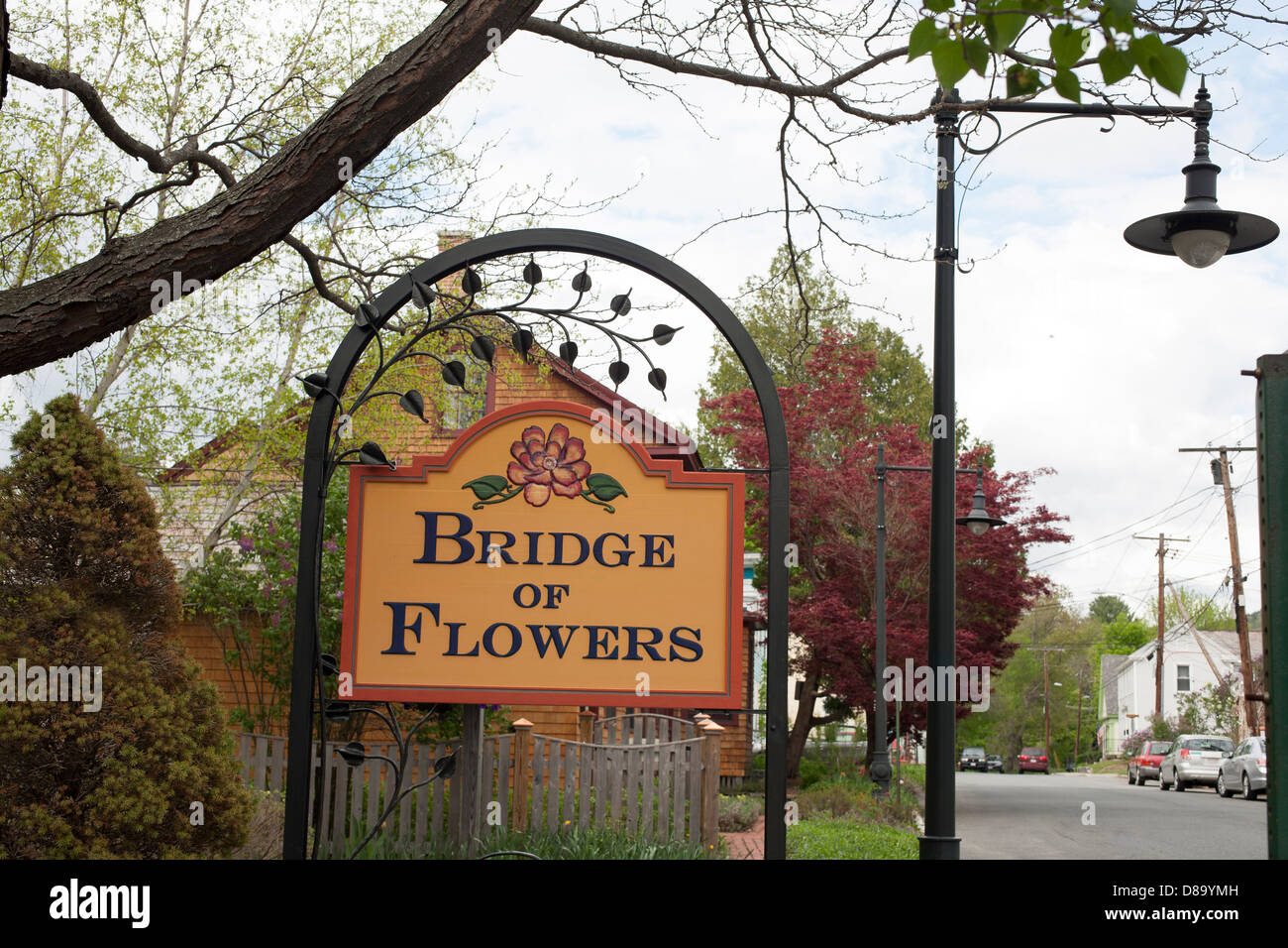 A carefully crafted sign announces the The calm Deerfield river reflects the  Shelburne Falls Bridge of Flowers. Stock Photo