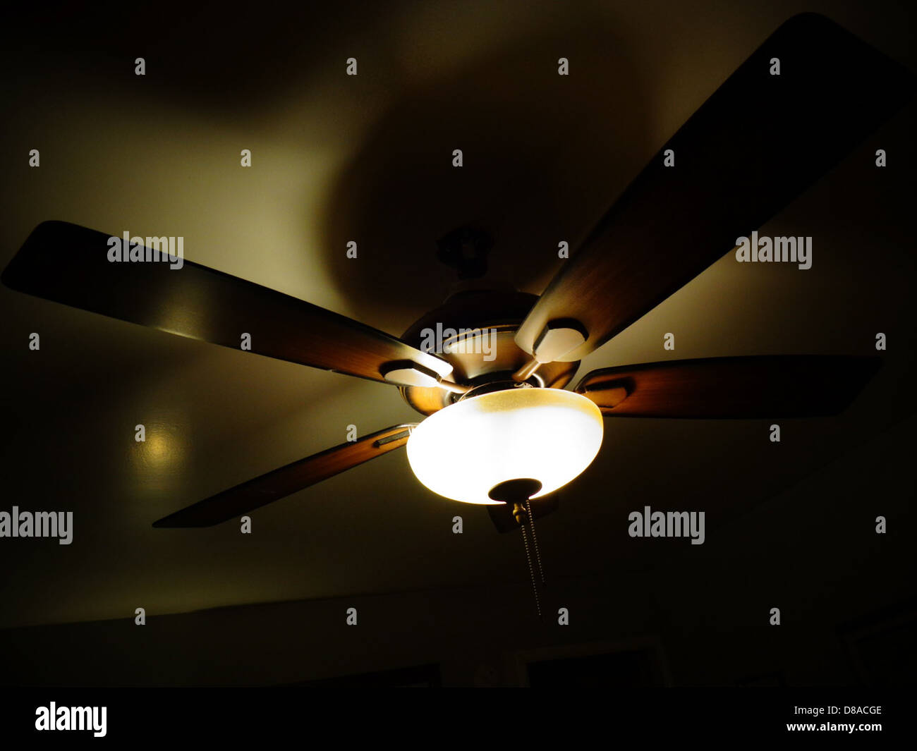 A ceiling fan with an integrated light fixture. The fan is shown in a well-lit room, offering both cooling and lighting functions to the indoor space. Stock Photo
