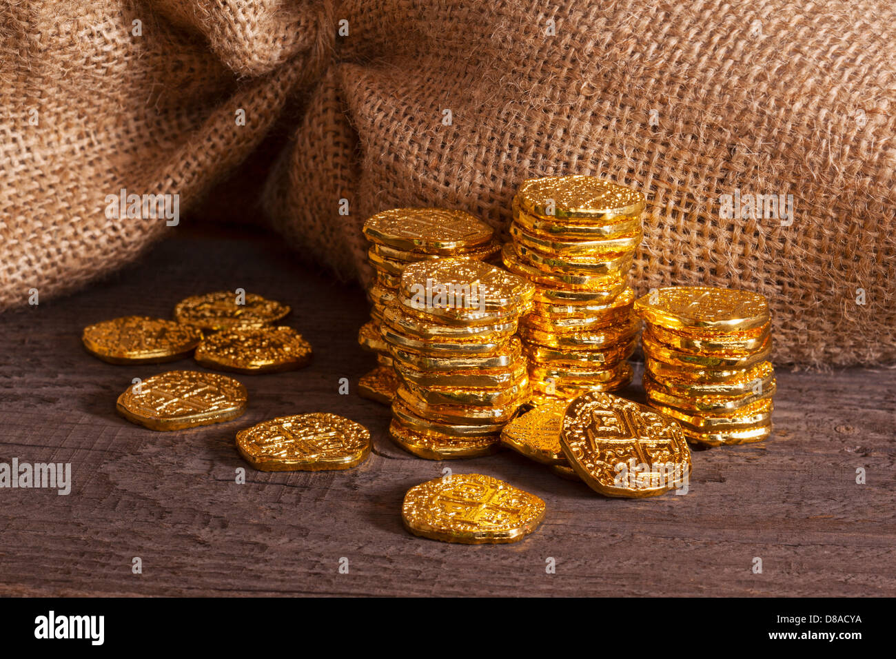 Doubloons and Sack gold doubloons stacked in front of burlap or jute sack on rustic wood