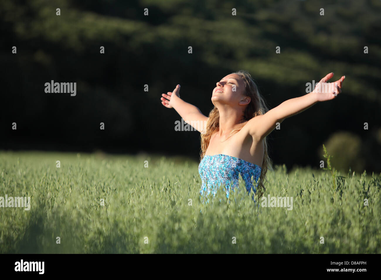 Beautiful teenager girl breathing happy with raised arms in a green meadow with a dark background Stock Photo