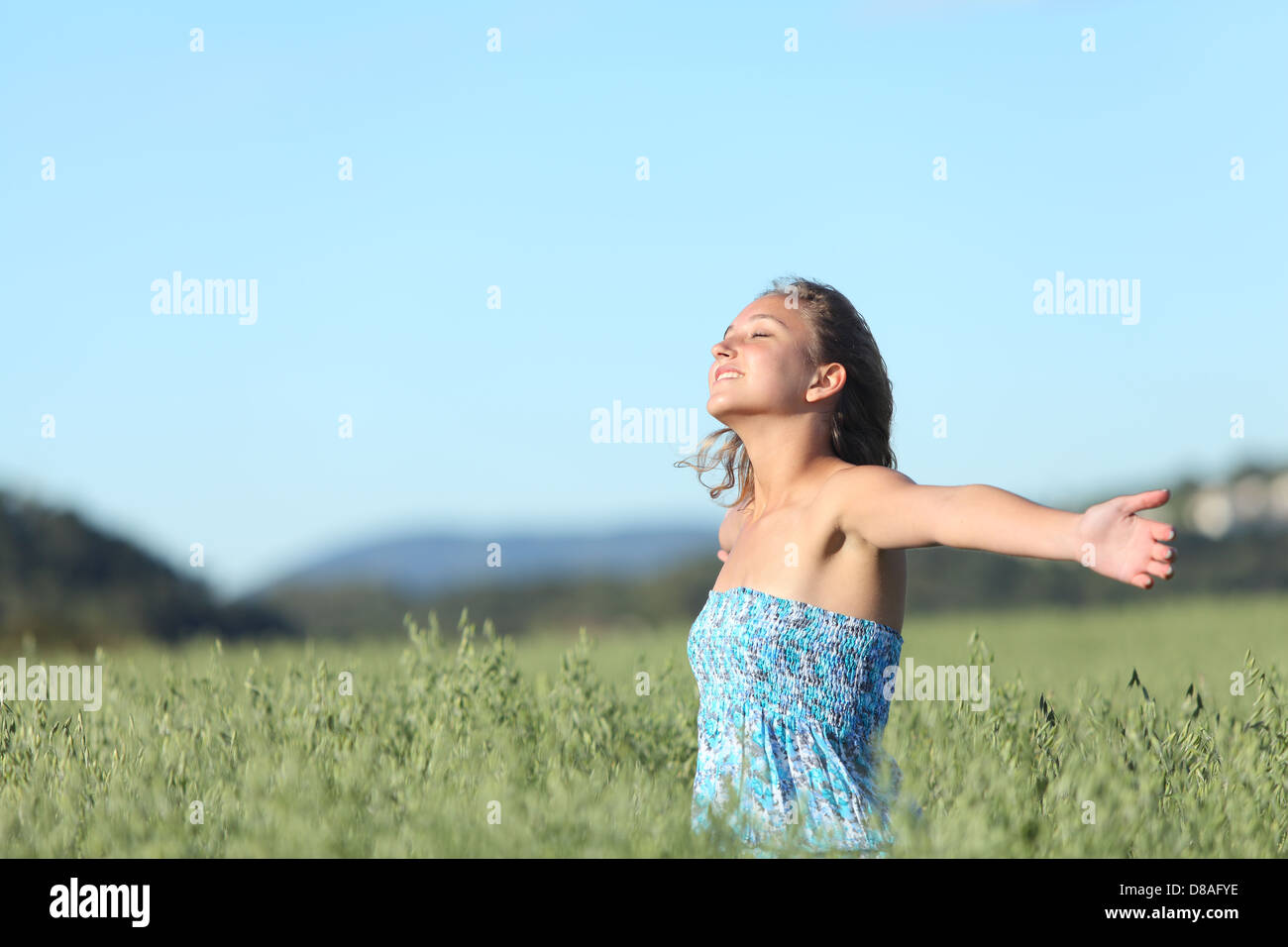 Beautiful woman breathing happy with raised arms in a green oat meadow with the blue sky in the background Stock Photo