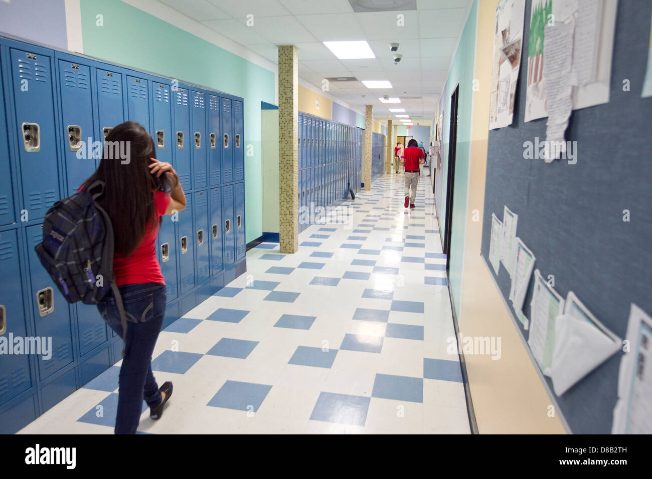 Female high school student wearing a backpack, walks down hallway with lockers at Austin, Texas school Stock Photo