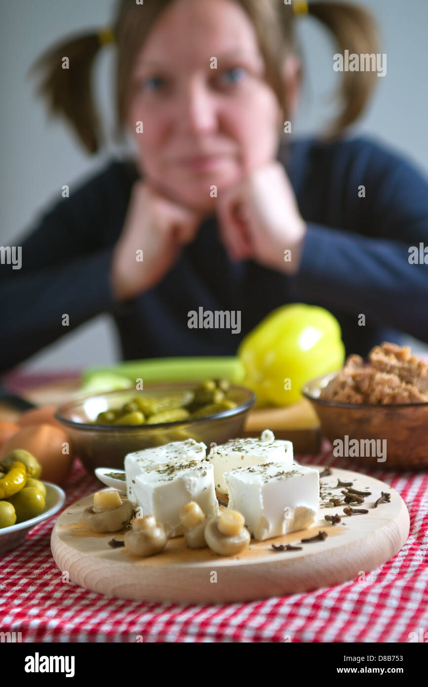 Feta cheese with mushrooms on a kitchen table. Woman with pigtails in the out of focus background. Stock Photo