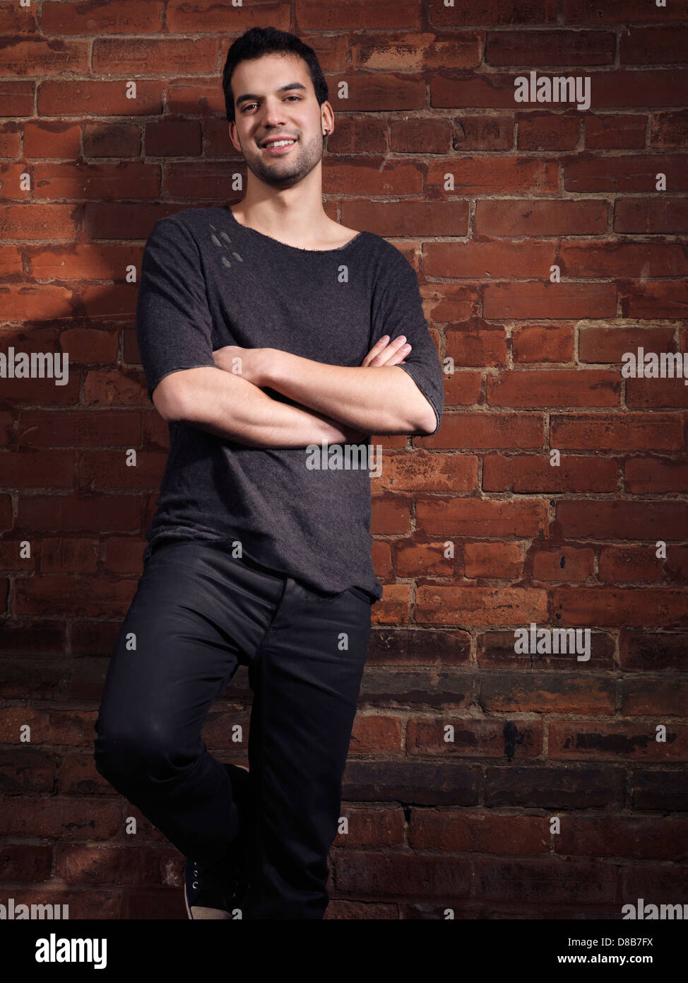 Expressive portrait of a smiling young man wearing black jeans and shirt standing at a brick wall Stock Photo