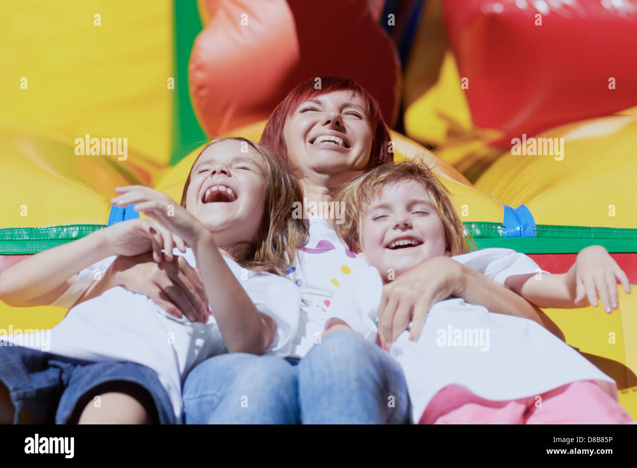 Mom and her daughters laughing out loud laying on a bouncing castle in a bright summer day outdoors. Lovely day! Stock Photo