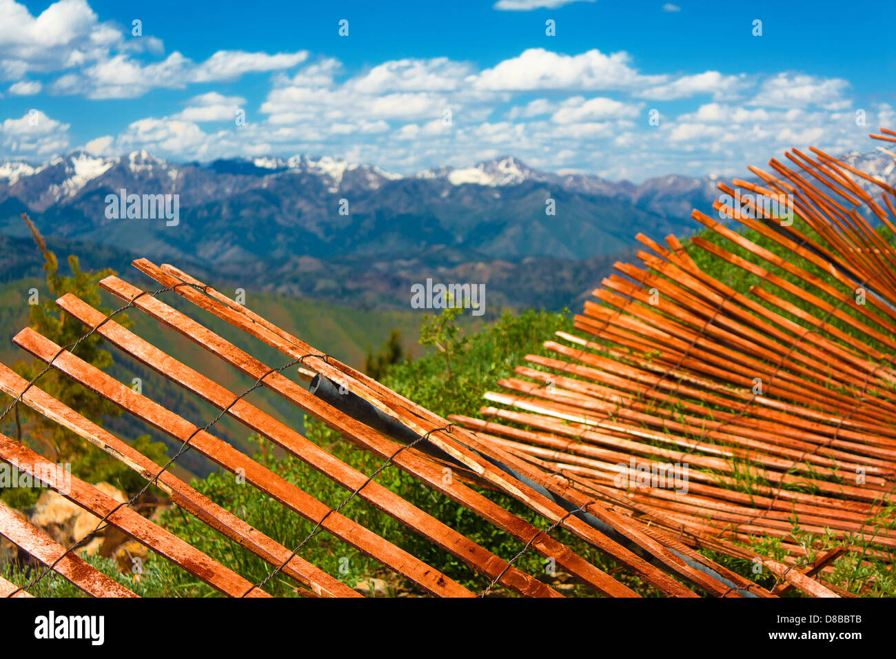 Orange wooden fence nearly falling down atop Bald Mountain in Sun Valley, Idaho, with snow-capped mountains in background Stock Photo