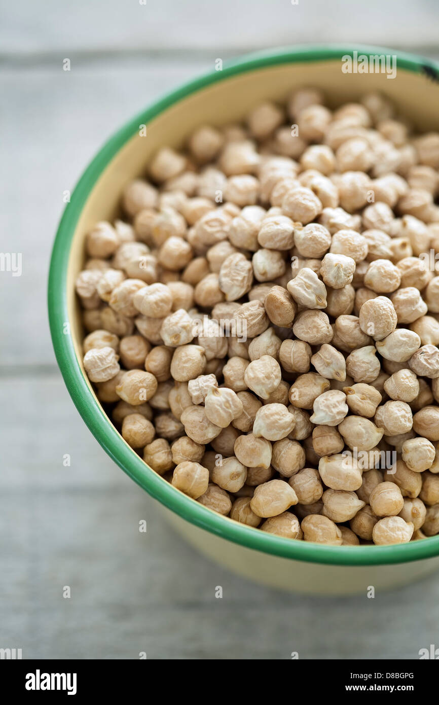 A large bowl of uncooked chickpeas on a rustic wooden table surface. Stock Photo