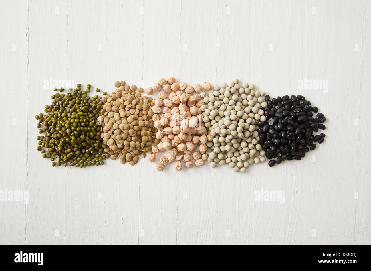 Piles of peas, beans, lentils, sprouts and pulses in a line on a rustic wood surface. Stock Photo