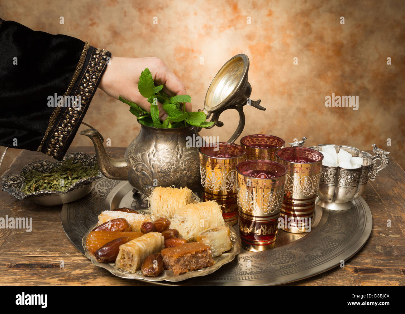 Female hand adding mint leaves to a tray with dates, cookies and tea the moroccan style Stock Photo