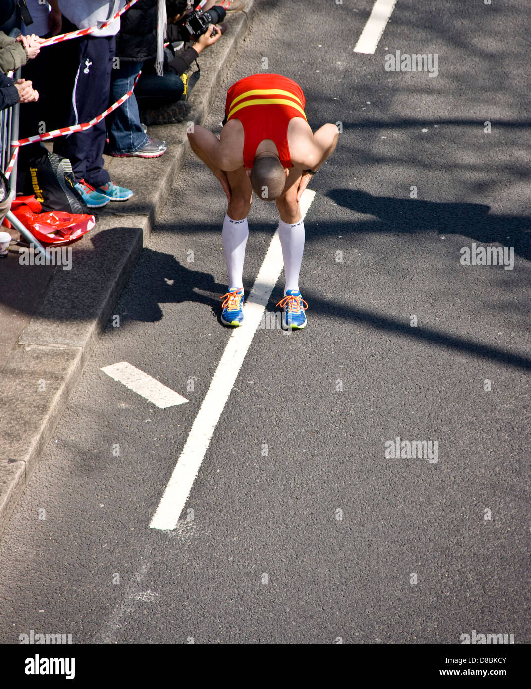 An exhausted runner competitor stops to stretch during 2013 London marathon England Europe Stock Photo