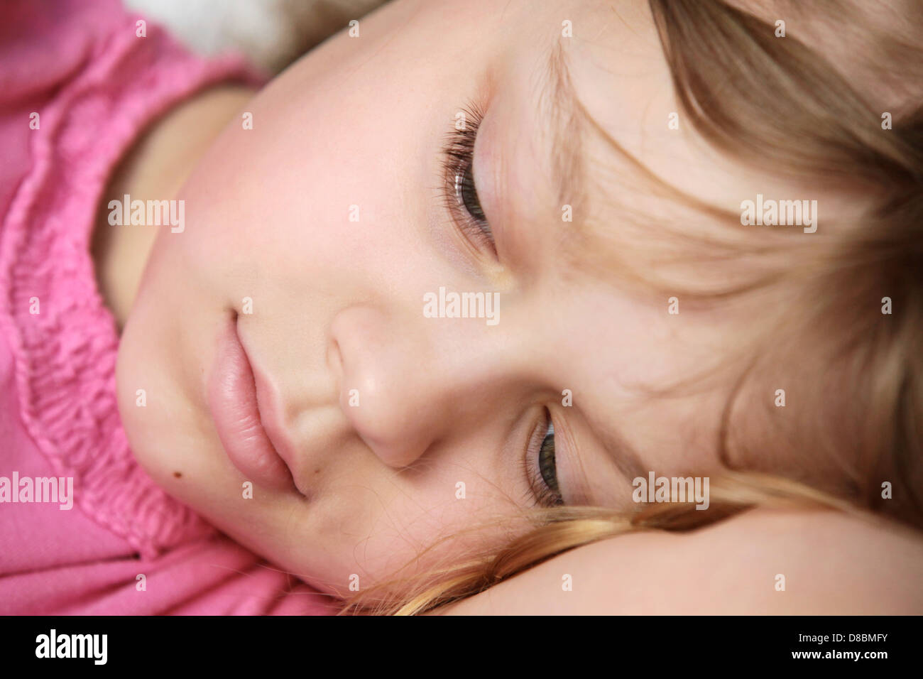 Closeup portrait of lying little blond Caucasian girl in pink Stock Photo